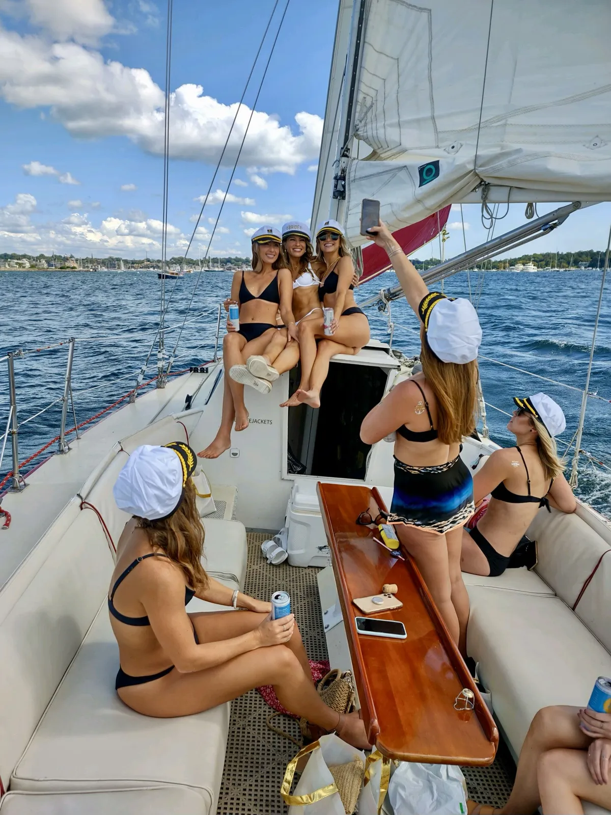 Group of women in bikinis and captain hats celebrating on a sailboat on a sunny day