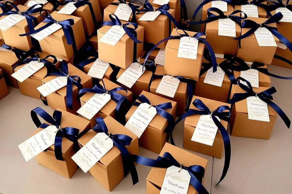 Rows of kraft paper wedding favor boxes with navy ribbons and thank-you gift tags arranged on a table.