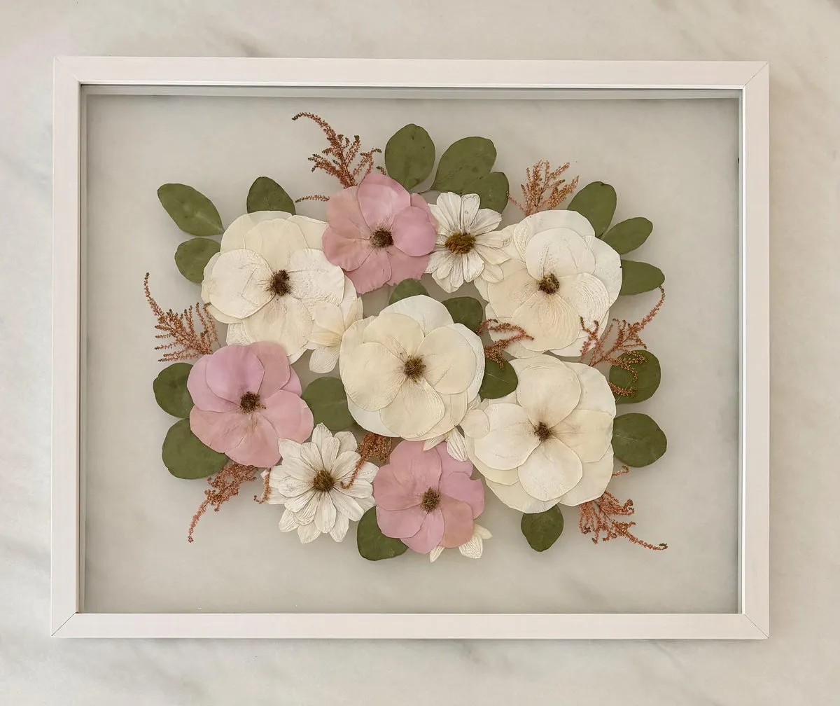 Pressed white and pink flowers arranged inside a white rectangular frame on a marble surface.