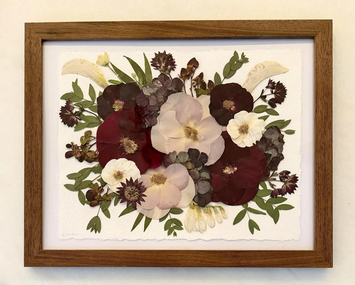 Framed pressed flower bouquet in burgundy, lavender, and white on deckle-edged paper in a wooden frame.