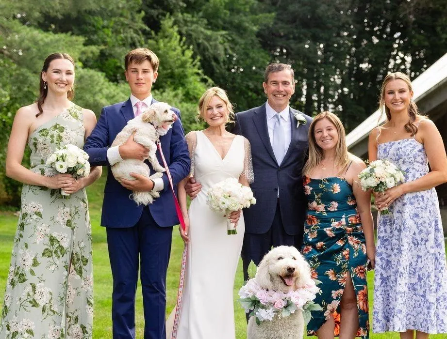 Bride and groom with family and two dogs posed on a green lawn outdoors.