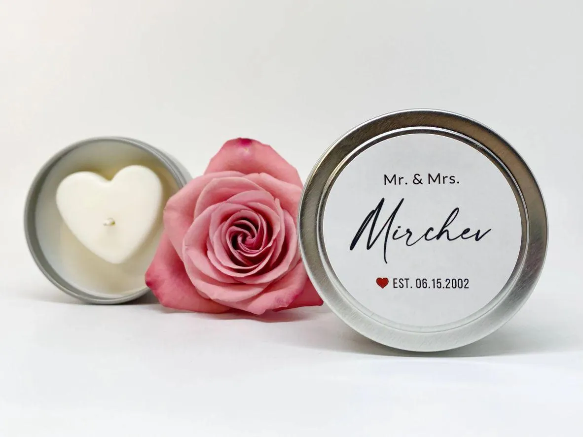 Personalized silver favor tins with a pink rose and heart-shaped candle on white.