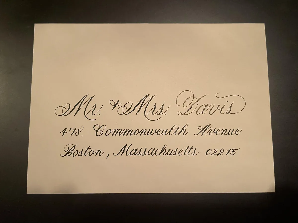 Cream envelope with black calligraphy address on a dark surface.