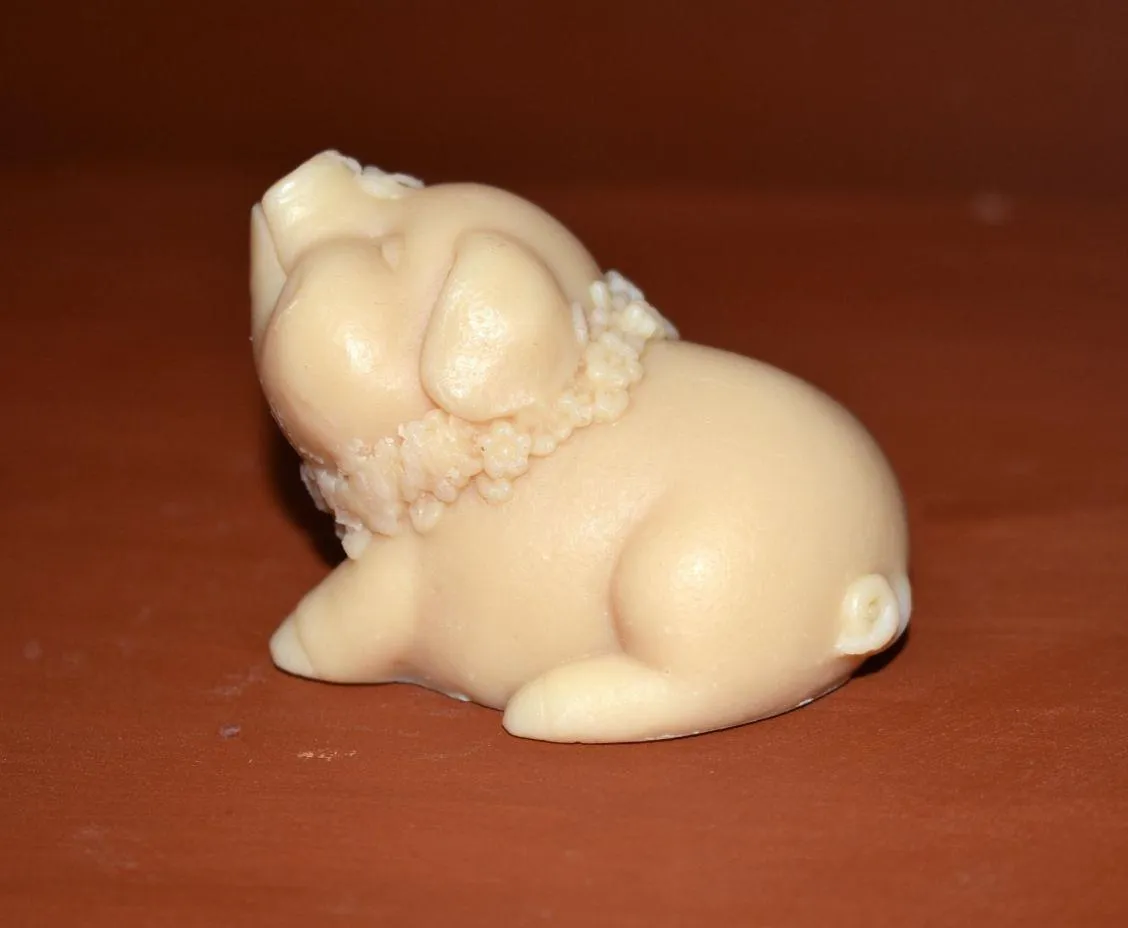 Small cream-colored sculpted pig figurine with a floral garland on a brown surface.