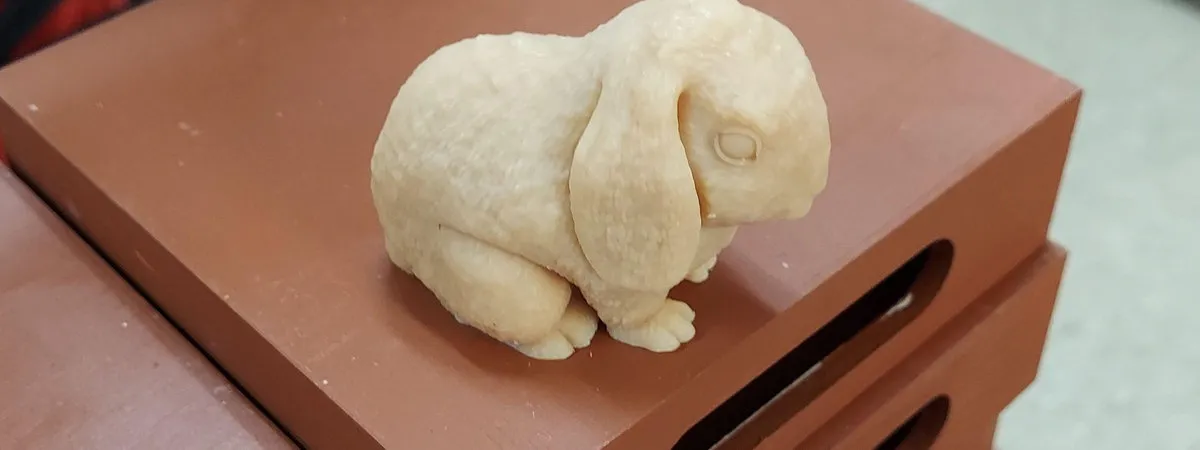 Close-up of a small cream-colored lop-eared rabbit figurine resting on a reddish-brown wooden surface.