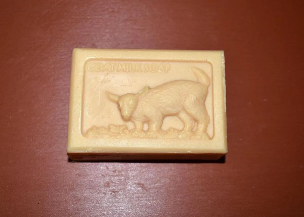 Rectangular bar of cream-colored goat milk soap with an embossed goat design on a reddish-brown surface.