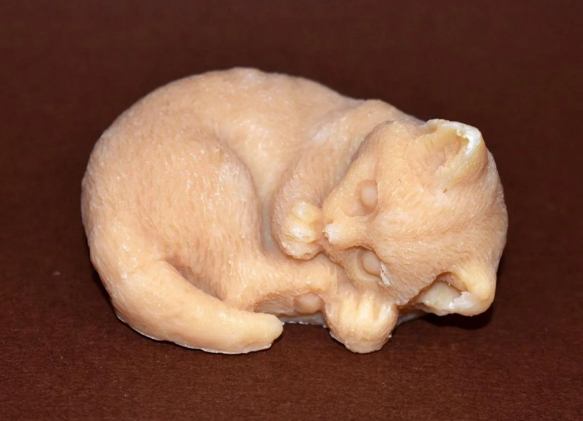 A small peach-colored figurine of a curled-up sleeping cat on a dark brown background.